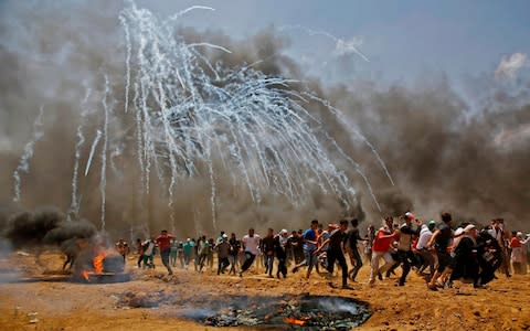 Palestinians run for cover as tear gas rains down near the border between Israel and the Gaza Strip - Credit: Mohammed Abed/AFP