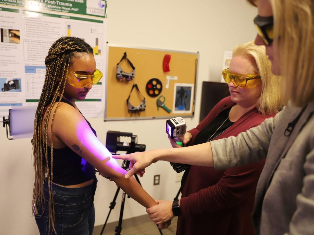 Katherine Scafide using violet light to observe bruising on a patient's arm