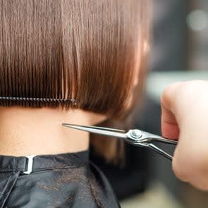 Hairdresser's hands are cutting brown short hair.