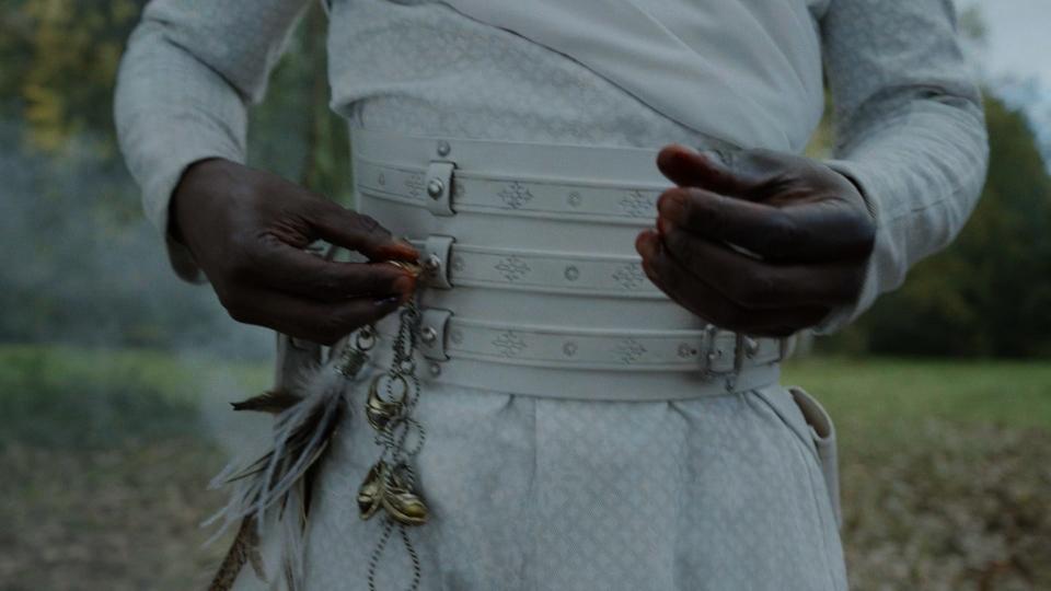 A close-up on Eamon Valda’s (Abdul Salis) midsection, clothed in white – he has a chain dangling from his white belt showing many Aes Sedai rings of different colors, including one he has just added, a yellow ring covered in blood