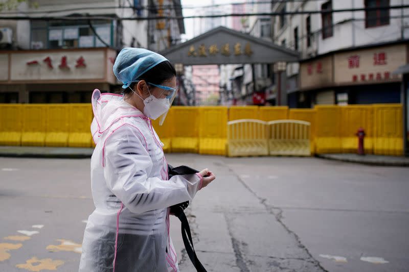 A woman wearing a face mask walks at a residential area blocked by barriers in Wuhan