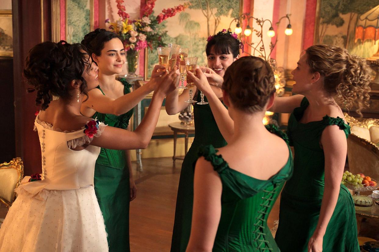 Circle of five young women wearing fancy gowns, raising their glasses in a toast.