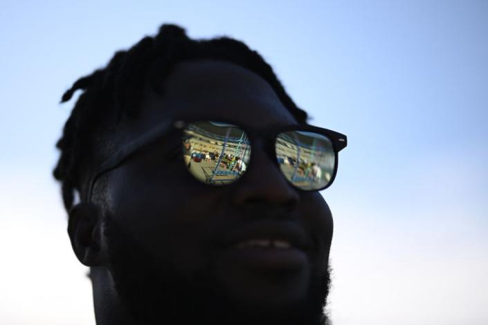 A man stands in the shade with bright reflections on his sunglasses.