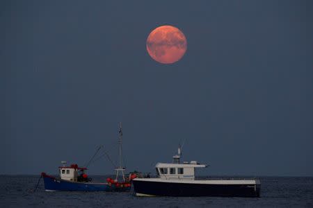 FILE PHOTO: The third supermoon of the year appears over fishing boats moored off Tenby Harbour in West Wales September 9, 2014. REUTERS/Rebecca Naden/File Photo