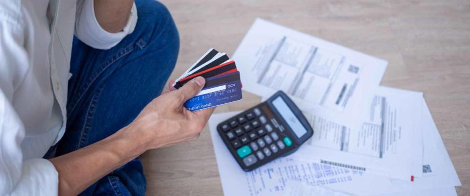 Man sitting on the ground with a pile of bills fanned out, holding onto a few credit cards.