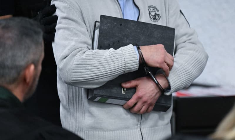 A Defendant Enters The Courtroom At The Higher Regional Court With Handcuffs And A File Folder Before The Start Of His Trial. The Two Defendants Are Alleged To Have Violated European Union Trade Restrictions In Connection With Deliveries Of Electronic Components For Military Equipment To Russia. Bernd Weißbrod/Dpa