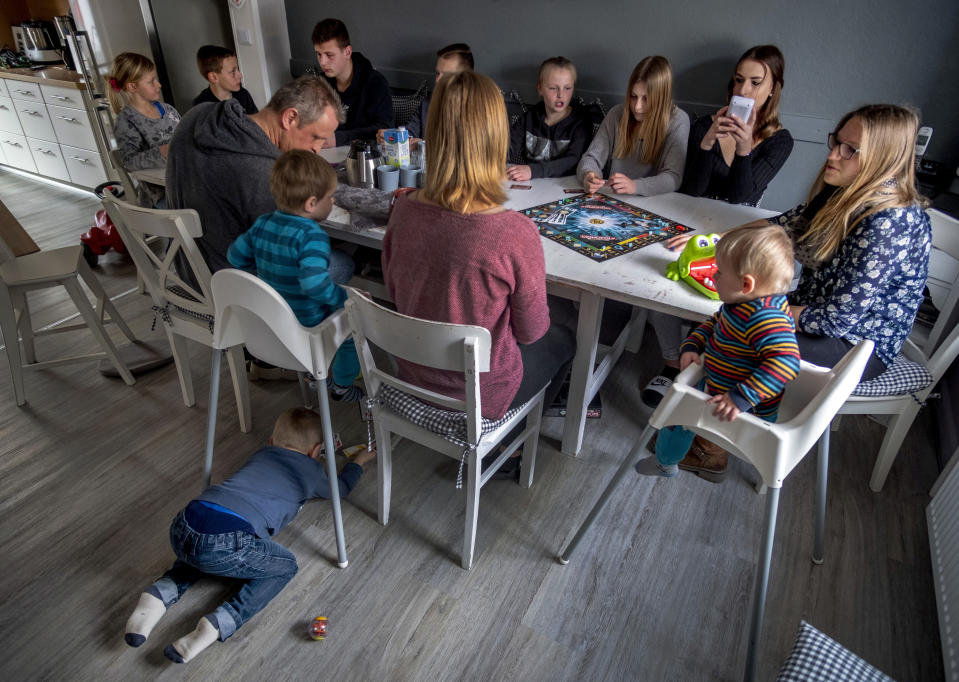 Katja Heimann, her husband and their eleven children sit around a table in their home in Eisemroth, central Germany, Thursday, March 25, 2021. One year into the coronavirus pandemic, Katja Heimann is still trying to keep her spirits up - despite several lockdowns and months of teaching seven of her children in home schooling. (AP Photo/Michael Probst)