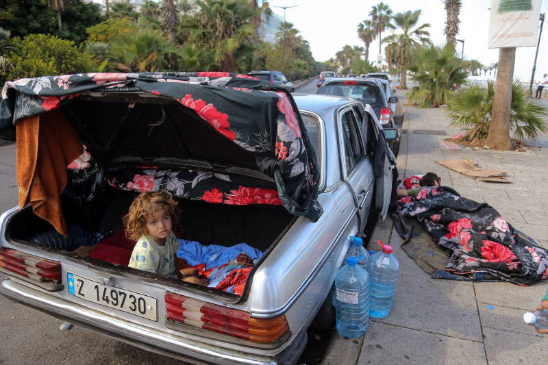 Abdel Salam Abdallah, a 10-year-old boy from the Lebanese southern town of Khiam sits in the trunk of his father's car after waking up from sleep. Abdel Salam's father is seen sleeping on the pavement of Beirut promenade. The Abdallah family consisting of four members are using the car as they makeshift home after fleeing Beirut southern suburb last week. Thousands of Lebanese and Syrian nationals fled south Lebanon and Beirut southern suburb following heavy Israeli air raids. Marwan Naamani/dpa