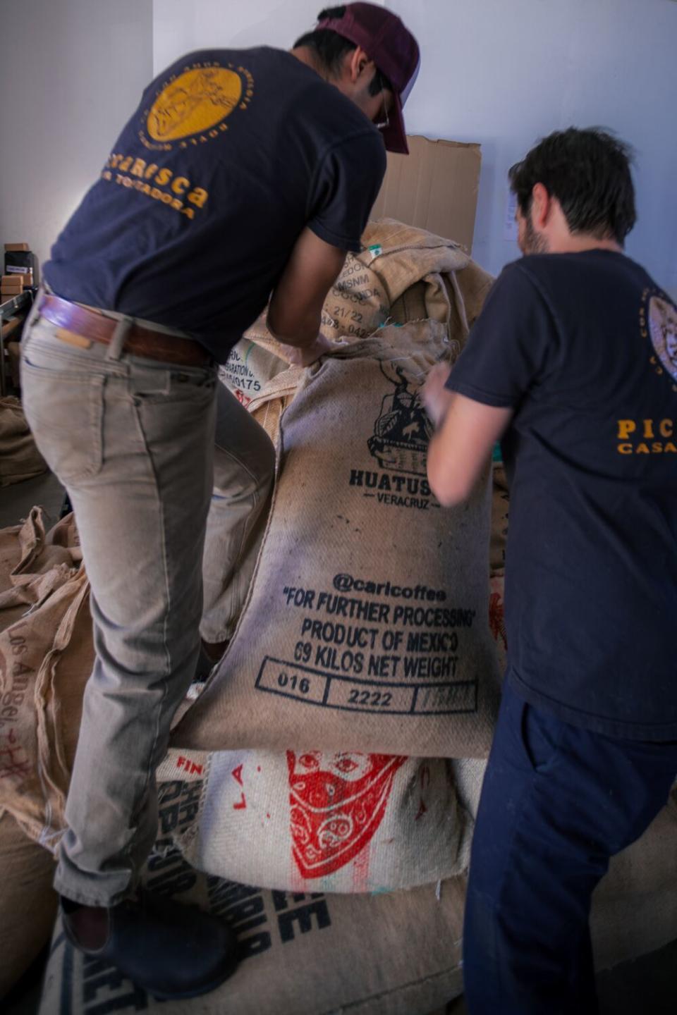 Leonardo Abularach and Pablo Peres Meza hoist bags of coffee beans.