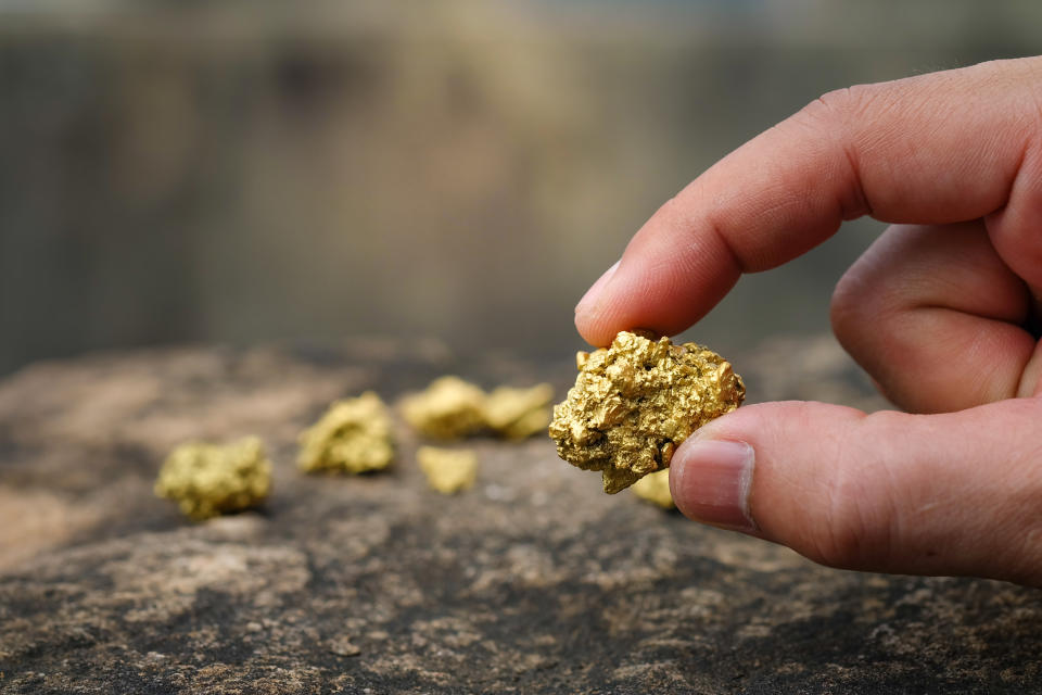 A hand holds a pure gold nugget.