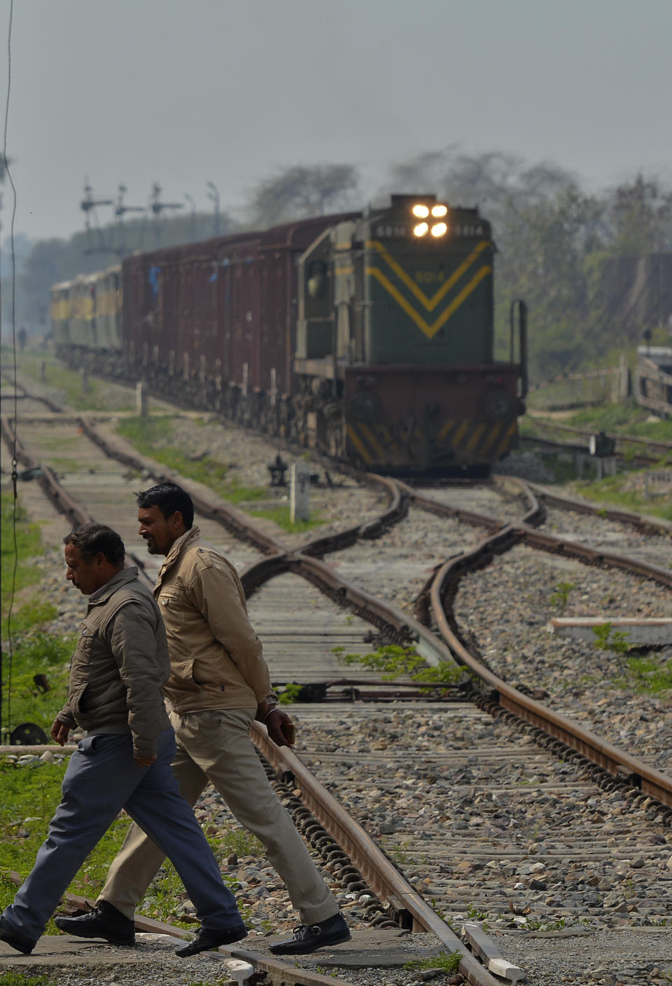 Two men cross the railway track as the Samjhauta Express train from Pakistan arrives in Atari, India, Monday, March 4, 2019. A Pakistani railway official said the key train service with neighboring India has resumed in another sign of easing tensions between the two nuclear-armed rivals since a major escalation last week over disputed Kashmir region. (AP Photo/Prabhjot Gill)