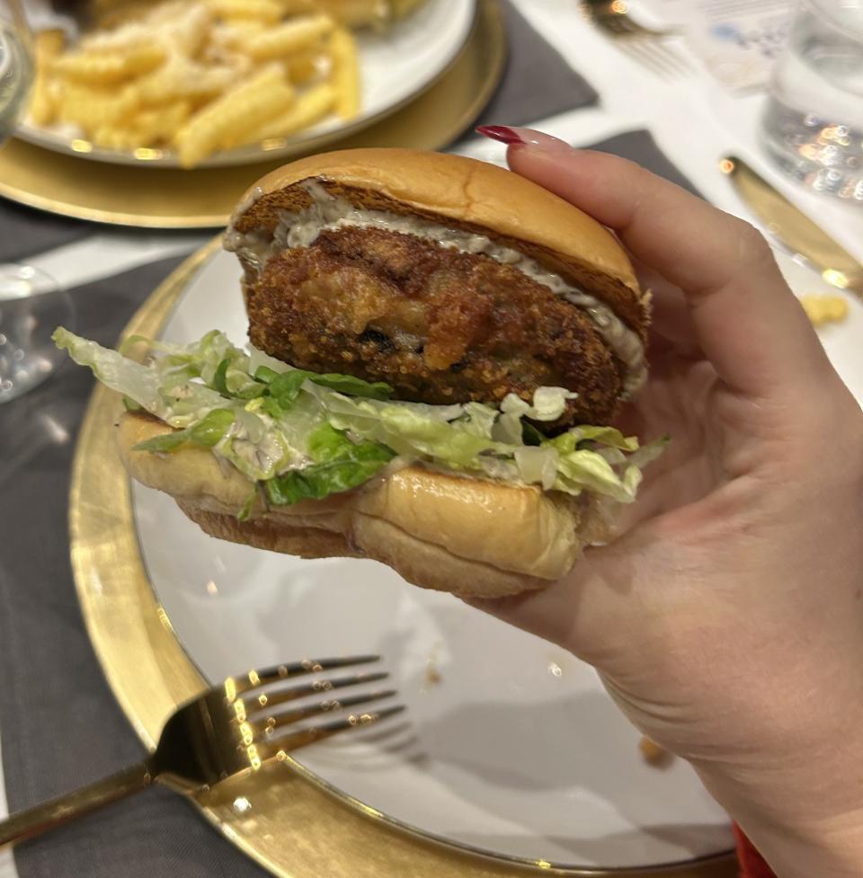 A hand holding the White Truffle 'Shroom Burger over a plate