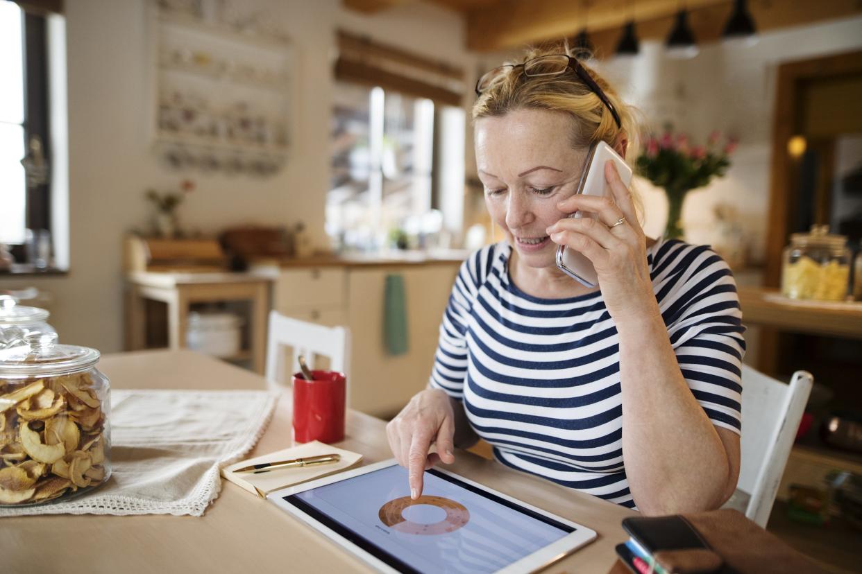 middle-aged woman at home working on tablet, making phone call