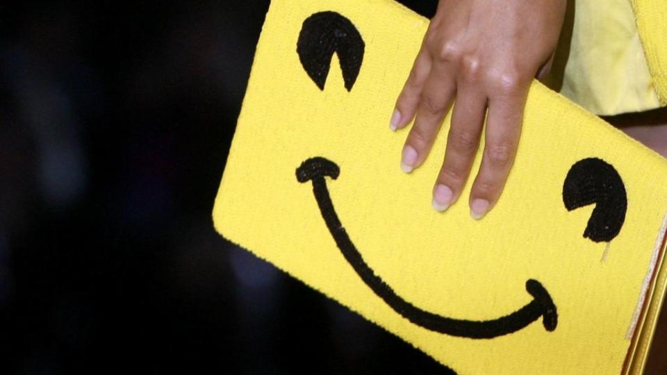 A model carries a smiling emoji purse