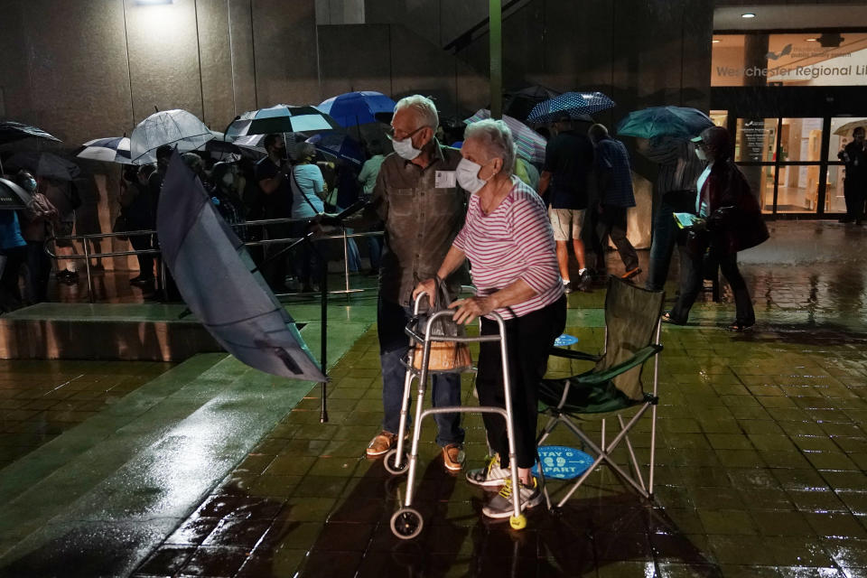 A couple stands in line as rain falls on voters waiting for the precinct to open, Monday, Oct. 19, 2020 in Miami. Florida begins in-person early voting in much of the state Monday. With its 29 electoral votes, Florida is crucial to both candidates in order to win the White House. (AP Photo/Lynne Sladky)