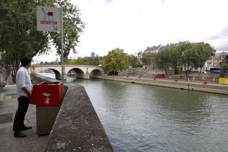 A journalist poses as he stands in front of a bright red, eco-friendly urinal on the Ile Saint-Louis along the Seine River in Paris, France, August 13, 2018. REUTERS/Philippe Wojazer