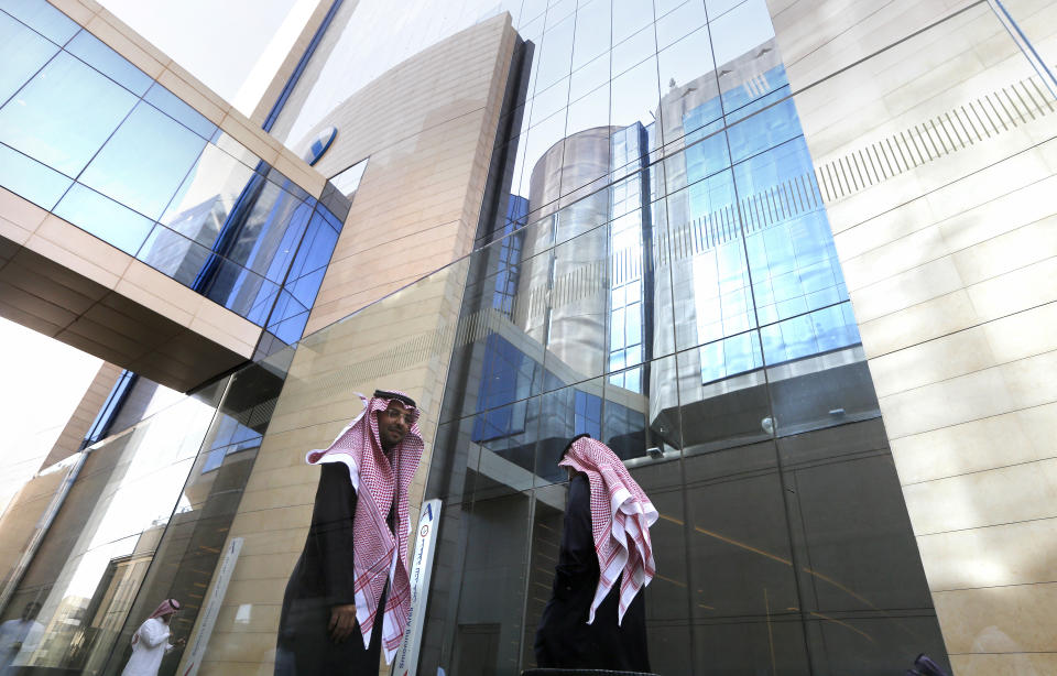 Saudi employees walk outside the Arab National Bank in Riyadh, Saudi Arabia, Thursday, Dec. 12, 2019. Shares in Saudi Aramco gained on the second day of trading Thursday, propelling the oil and gas company to a more than $2 trillion valuation where it holds the title of the world's most valuable listed company. (AP Photo/Amr Nabil)