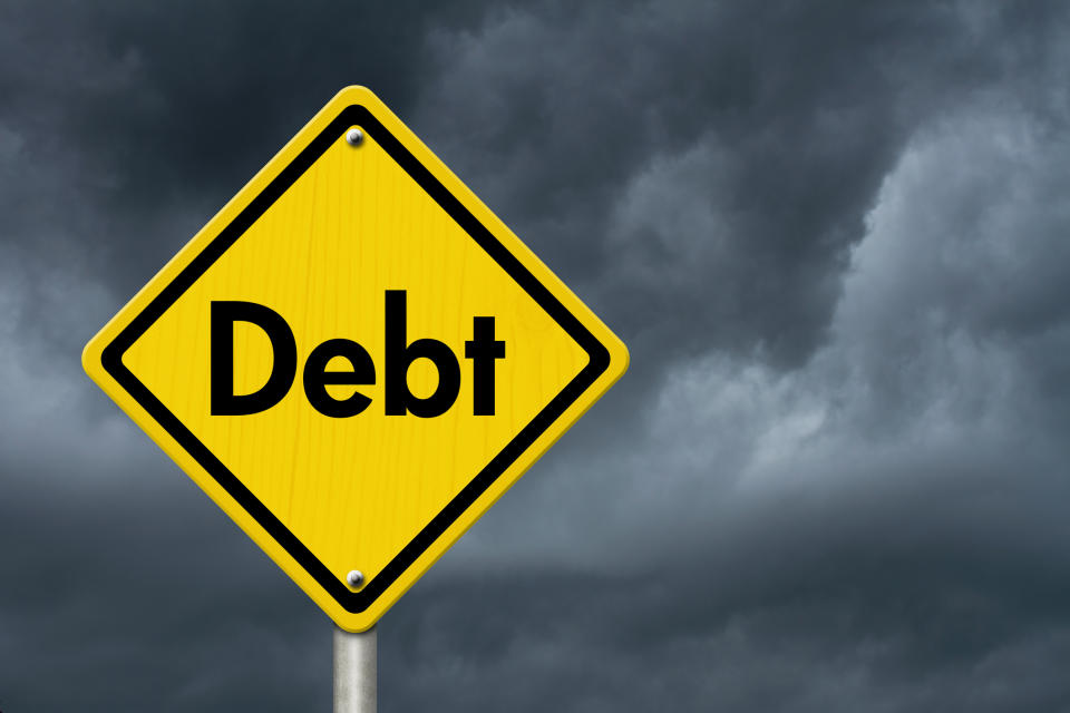 Yellow diamond-shaped road sign with the word debt with a backdrop of dark, gray skies