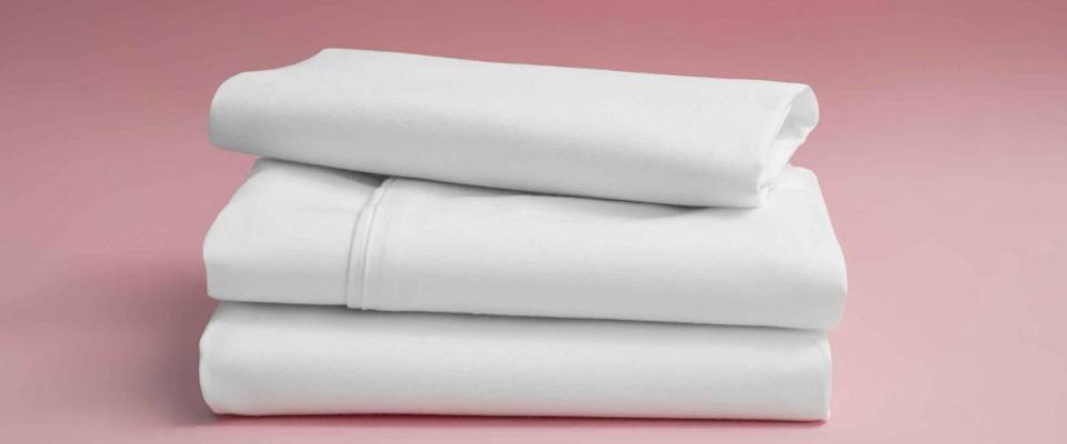 Stack of white bedding against pink backdrop, folded soft bed clothes, stack of white cotton sheets on a pink background for advertising, commercial and mock up