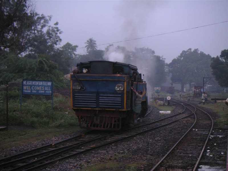 The 'X' Class steam Rack Locomotive arrives from its shed to take charge of the 662SR up to Coonoor while a signboard welcomes passengers to the Nilgiri Mountain Railway.