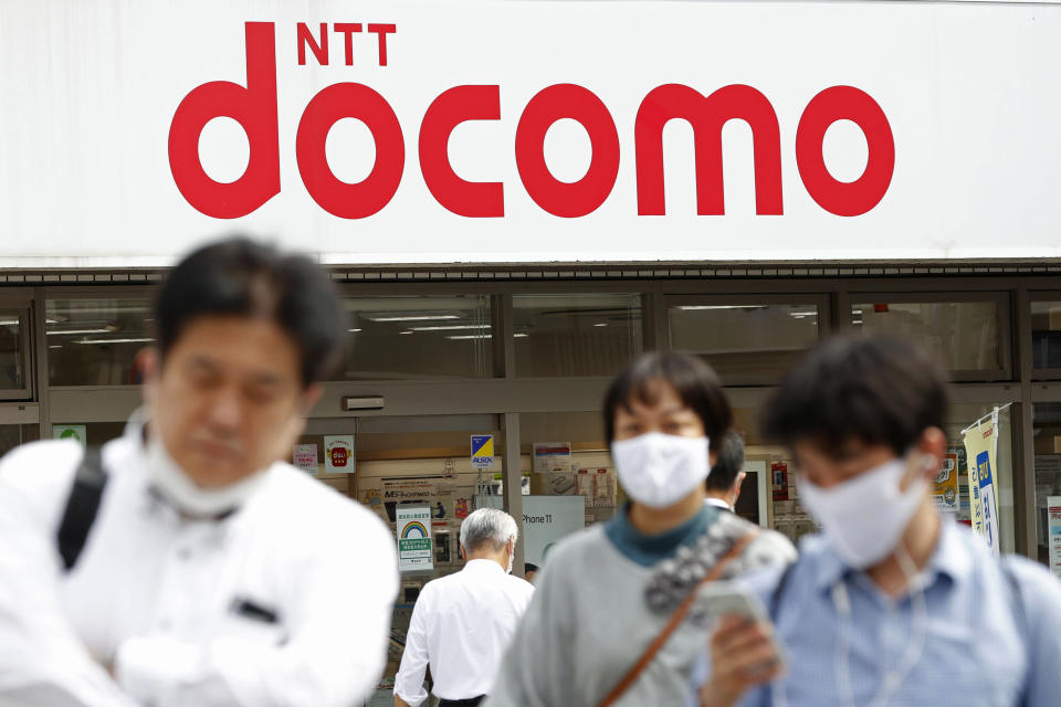 Passers-by walk past a NTT DoCoMo shop in Tokyo, Tuesday, Sept. 29, 2020. Shares in Japanese telecoms giant Nippon Telegraph & Telephone, or NTT, fell Tuesday on news it is preparing for a takeover of its mobile phone carrier NTT DoCoMo. (Kyodo News via AP)