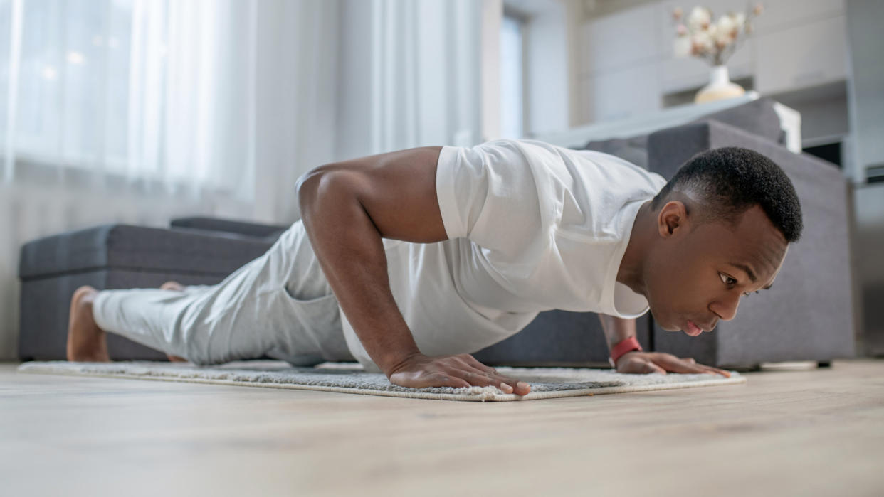  Young African american person in white clothes exercising at home. 