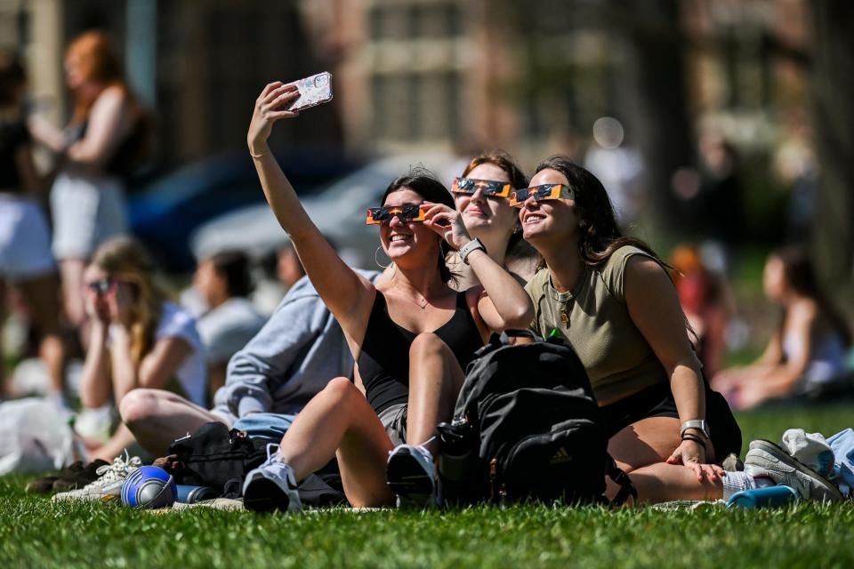 A group takes a selfie with eclipse glasses on while taking in the solar eclipse on the lawn next to Michigan State University's Cowles House on Monday, April 8, 2024, on the MSU campus in East Lansing.