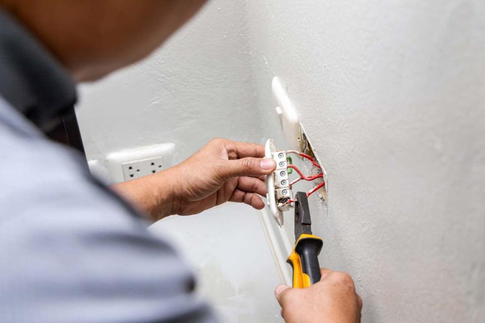 A close up of a person using a tool to fix electrical components in a wall.
