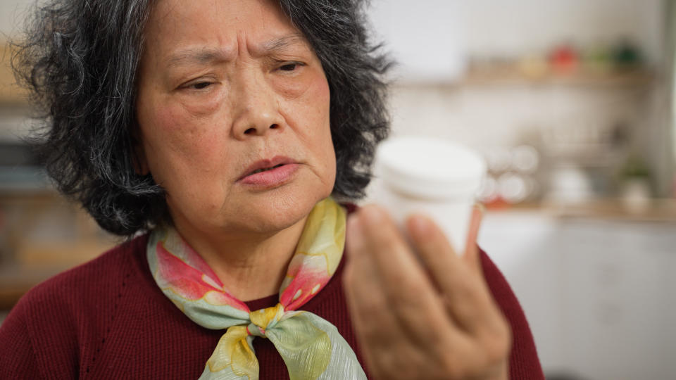 Una donna aggrotta la fronte mentre guarda il flacone di prescrizione che ha in mano, apparendo ansiosa o confusa