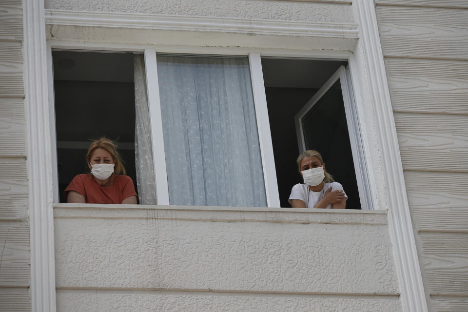 In this Friday, May 15, 2020 photo, Betul Sahbas, 47, right, who had been experiencing COVID-19 symptoms, looks from her flats's window in Istanbul as a contact tracing team with Turkey's Health Ministry's coronavirus contact tracing team, arrives to swab her and take a sample. Thousands of tracers are going house to house nationwide to test and inform patients on isolation. Sahbaz, started showing symptoms after her flatmate tested positive. "I was scared and panicked, sure we hear about it, but it's different when you experience it" she explained. People who test positive are required by law to self-quarantine and are tracked by a phone application. (AP Photo/Emrah Gurel)