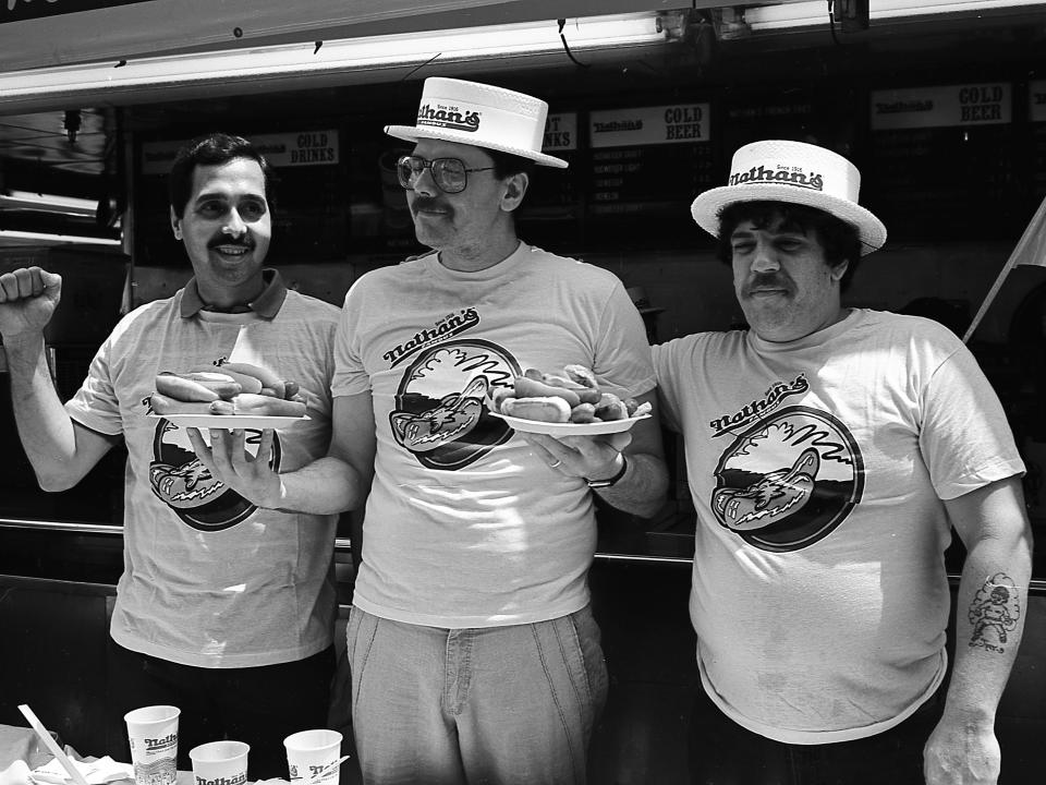 Portrait of three, unidentified contestants as they pose with plates of hot dogs prior to the 1987 Nathan's Hot Dog Eating Contest at Coney Island
