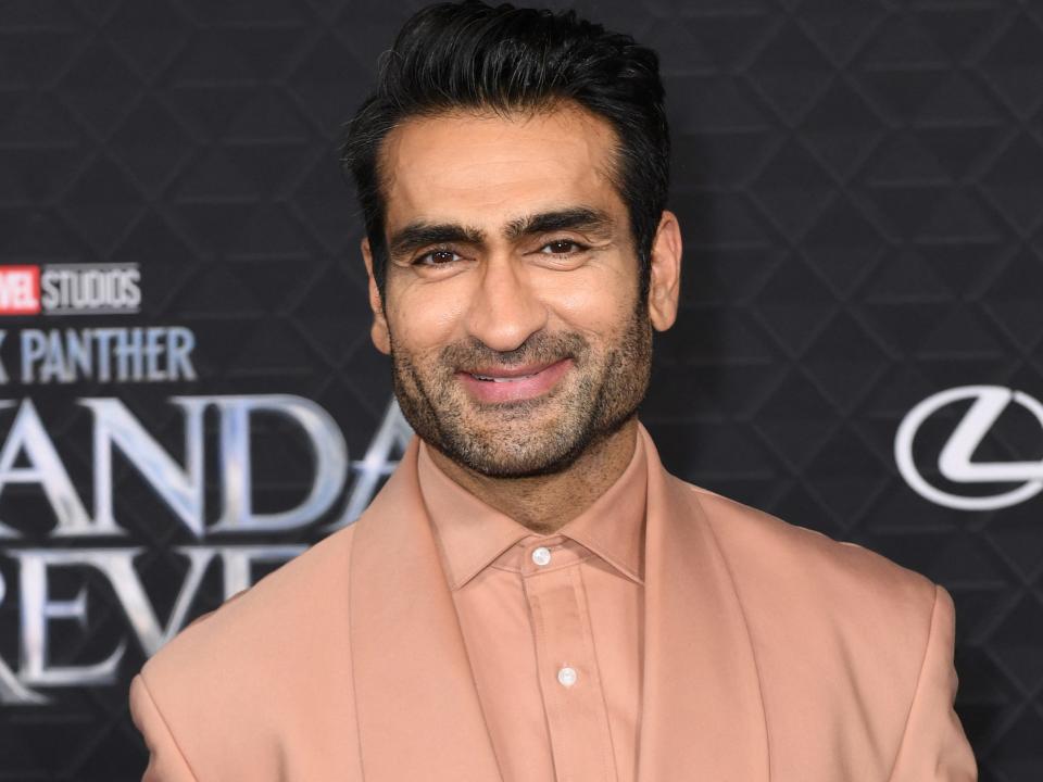 Kumail Nanjiani poses for photos on the red carpet in a salmon-colored suit.