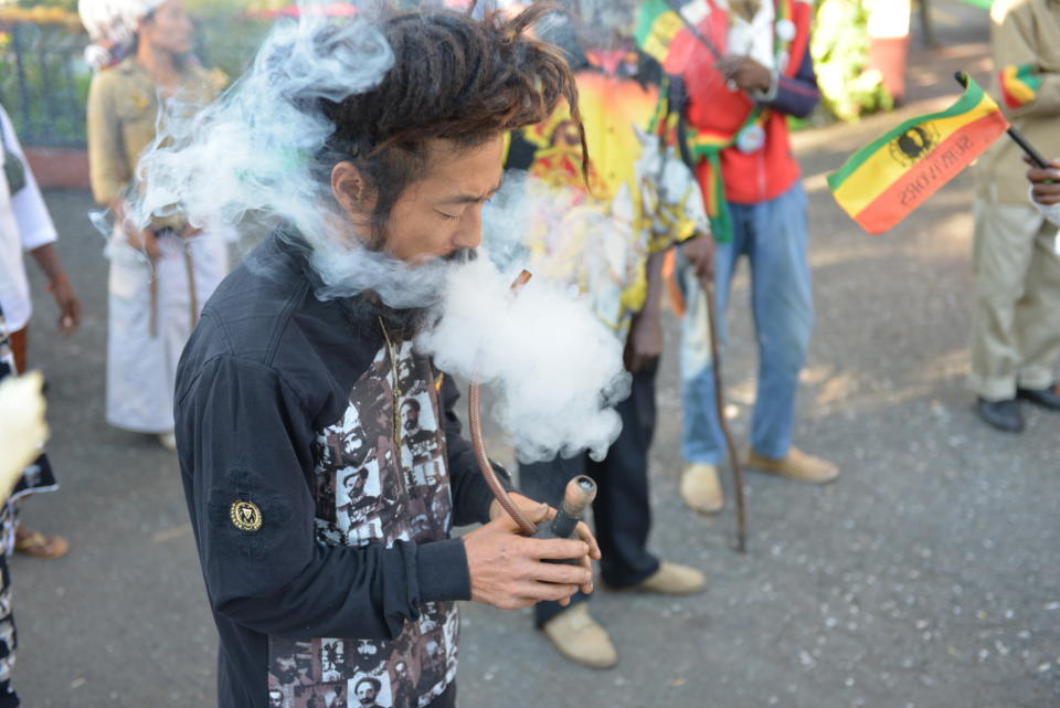 In this Feb. 6, 2013 photo, a Rastafarian named Bongho Jatusy smokes a pipe of marijuana outside a museum dedicated to the memory of late reggae icon Bob Marley in Kingston, Jamaica. While marijuana is still illegal in Jamaica, where it is known popularly as “ganja,” increasingly vocal advocates say that Jamaica could give its struggling economy a boost by taking advantage of the fact the island is nearly as famous for its marijuana as it is for beaches, reggae music and world-beating sprinters. (AP Photo/David McFadden)