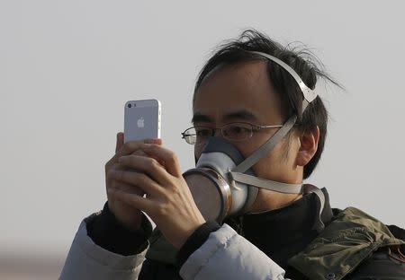 A man wearing a mask takes a picture with his iPhone at the Tiananmen Square during a heavily polluted day in Beijing, China, November 29, 2015. REUTERS/Kim Kyung-Hoon