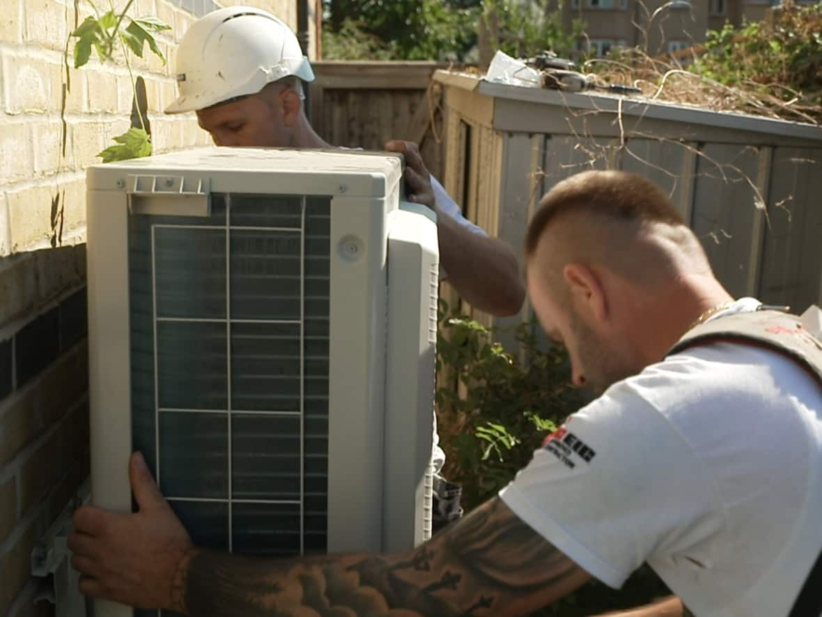 Air conditioning installers attach the outer part of the unit to the exterior of a North London flat. (J.F. Bisson/CBC - image credit)