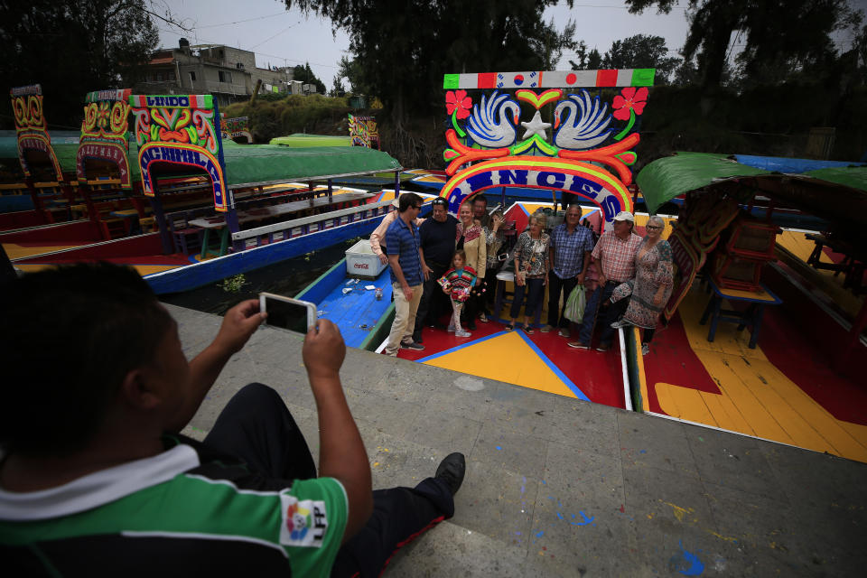 A gondolier takes a photo for a group of Americans after they took a ride on a trajinera, colorful passenger boats typically rented by tourists, families, and groups of young people, in Xochimilco, Mexico City, Friday, Sept. 6, 2019. The usually festive Nativitas pier was subdued and largely empty Friday afternoon, with some boat operators and vendors estimating that business was down by 80% on the first weekend following the drowning death of a youth that was captured on cellphone video and seen widely in Mexico. Borough officials stood on the pier to inform visitors of new regulations that went into effect Friday limiting the consumption of alcohol, prohibiting the use of speakers and instructing visitors to remain seated.(AP Photo/Rebecca Blackwell)