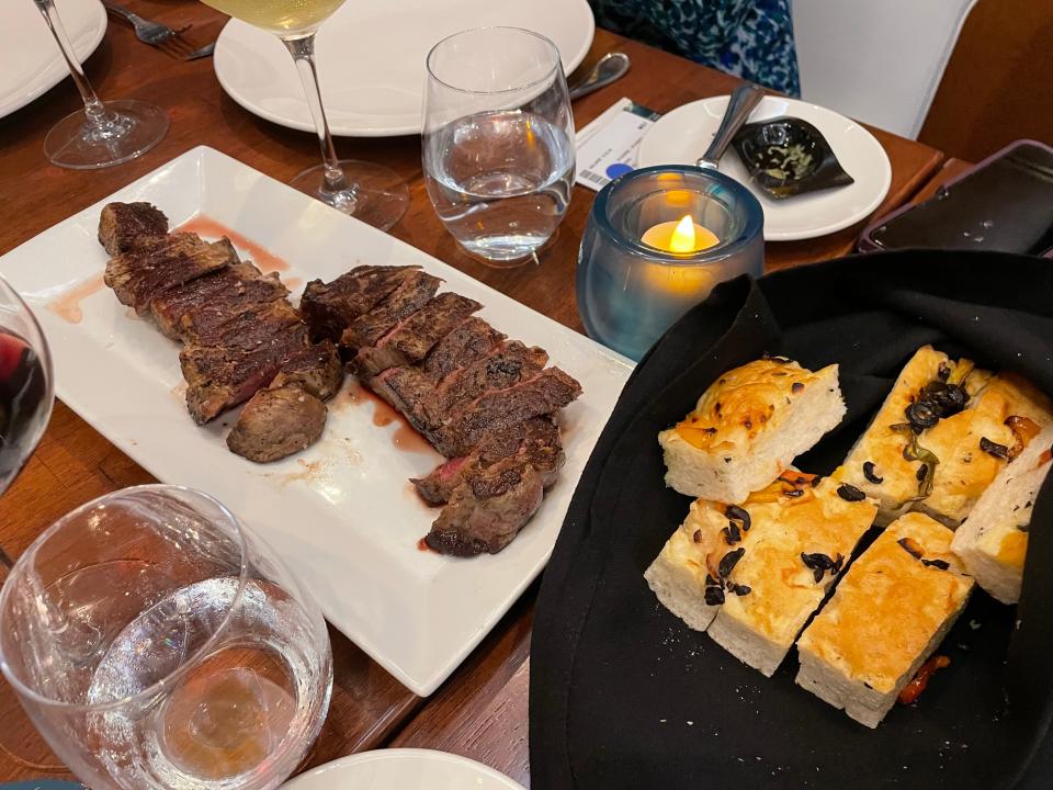 Steak on a plate and bread in a basket surrounded by dinnerware at JWB Prime Steakhouse on the Margaritaville at Sea Paradise.