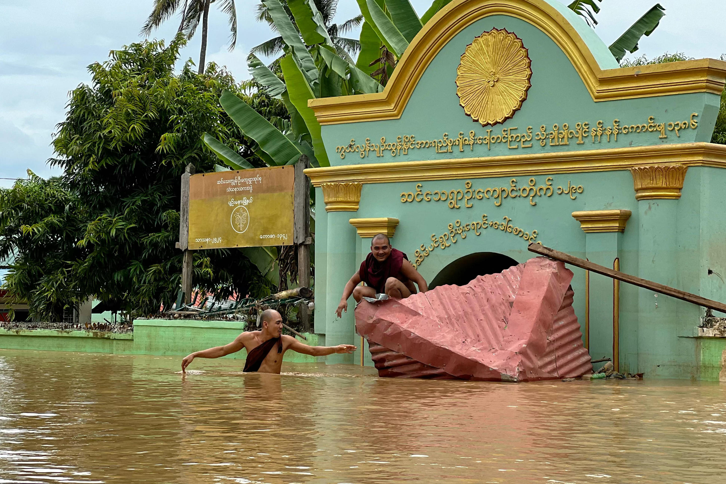 A Buddhist monk wades through flood waters as another sits on a broken roof in front of a monastery in Sin Thay village in Pyinmana, in Myanmar's Naypyidaw region, on September 13, 2024. (Sai Aung Main/AFP via Getty Images)