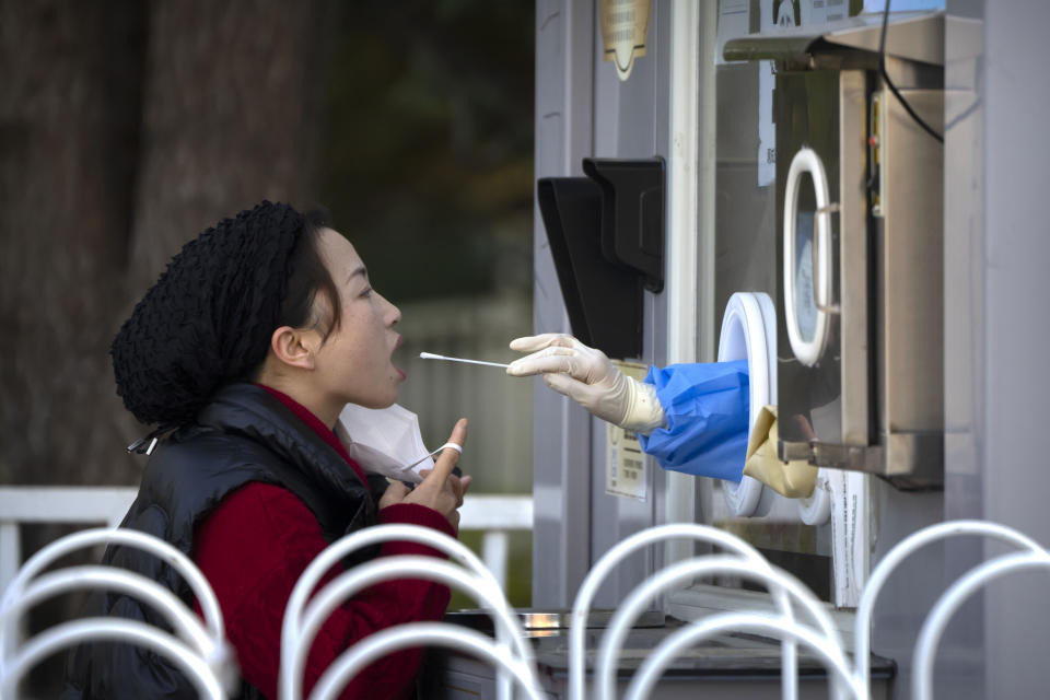 A woman has her throat swabbed for a COVID-19 test at a coronavirus testing site in Beijing, Tuesday, Nov. 1, 2022. Shanghai Disneyland was closed and visitors temporarily kept in the park for virus testing, the city government announced, while social media posts said some amusements kept operating for guests who were blocked from leaving. (AP Photo/Mark Schiefelbein)