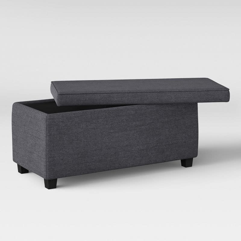 Dark fabric upholstered storage ottoman with raised lid displaying interior compartment