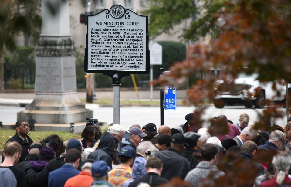 People stand under a North Carolina highway historical marker to the 1898 Wilmington Coup shortly after it was unveiled during a dedication ceremony in downtown Wilmington on Friday, November 8, 2019. The marker stands outside the Wilmington Light Infantry building, the location where a mob of white supremacists originally gathered.