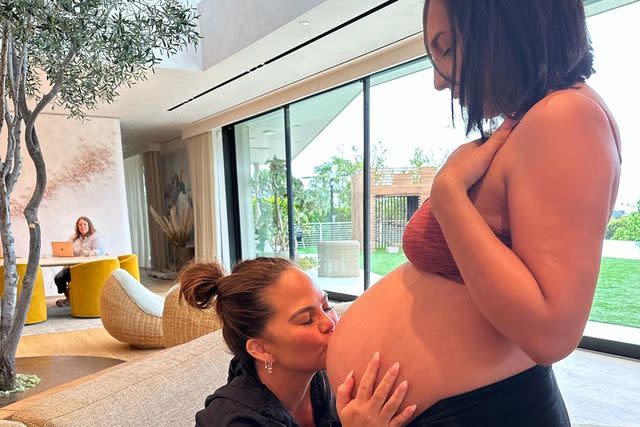 <p>Chrissy Teigen/Instagram</p> Chrissy Teigen kissing surrogate's bump