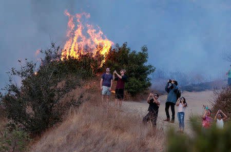 Spectators watch a helicopter fly over the La Tuna Canyon fire over Burbank. REUTERS/ Kyle Grillot