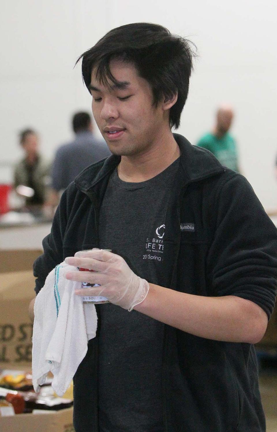Cuyahoga Falls Chick-Fil-A employee Christian Le cleans a can of donated food as he and his fellow coworkers volunteer Monday at the Akron-Canton Regional Foodbank.