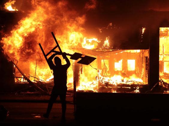 A man holds up a sign near a burning building during protests sparked by the death of George Floyd while in police custody (Getty)