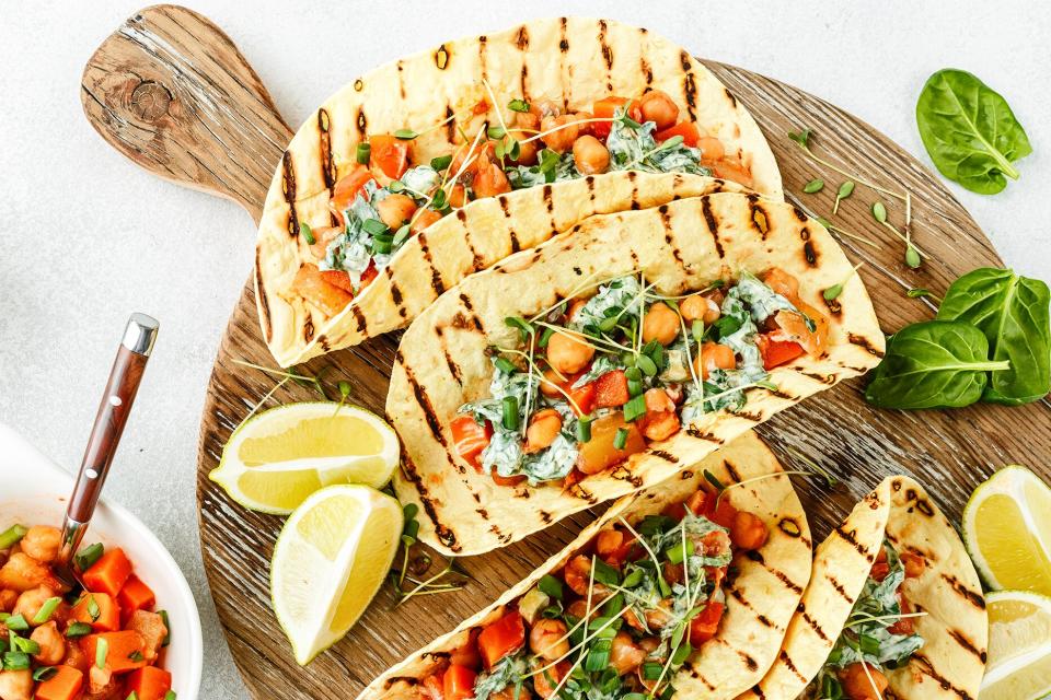 vegetarian snack of tacos with chickpea curry and sour cream sauce with parsley, spinach, green onions and sprouted flax seeds. healthy plant based food. top view on light background, flat lay