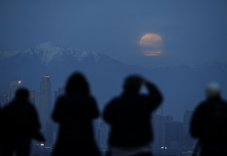 People watch the supermoon rise behind the downtown Los Angeles skyline, from Kenneth Hahn Park in Los Angeles, Sunday, Jan. 20, 2019. The year's first supermoon, when a full moon appears a little bigger and brighter thanks to its slightly closer position to Earth, is one of two lunar events Sunday. If skies are clear, a total eclipse will also be visible in North and South America, and parts of Europe. (AP Photo/Ringo H.W. Chiu)