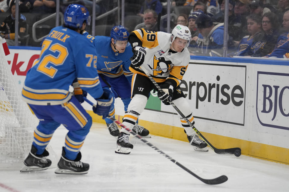 Pittsburgh Penguins' Jake Guentzel (59) chases after a loose puck along the boards as St. Louis Blues' Colton Parayko and Justin Faulk (72) defend during the third period of an NHL hockey game Saturday, Oct. 21, 2023, in St. Louis. (AP Photo/Jeff Roberson)