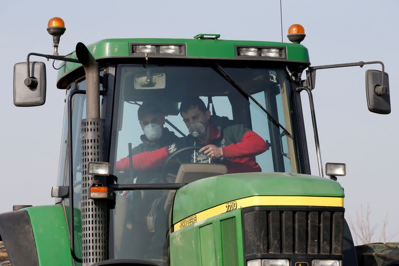 FILE PHOTO: A French farmer wearing a protective face mask gives a driving lesson to a new young farm worker for his tractor in Anneux, France