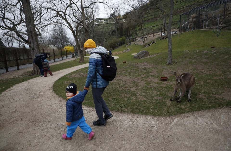 Visitors walk past a kangaroo at an enclosure at the zoo in Prague, Czech Republic, Monday, April 12, 2021. The Czech government has agreed to start easing the tight lockdown, caused by the COVID-19 pandemic, in one of the hardest-hit European countries. Children up to the fifth grade will be back at schools while the stores selling clothes and shoes for kids, laundries, outdoor farmers markets, zoo and botanical gardens are reopened. (AP Photo/Petr David Josek)